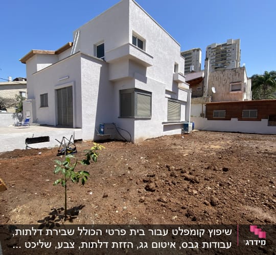 בית לבן עם אדמה חומה ועץ קטן בחצר